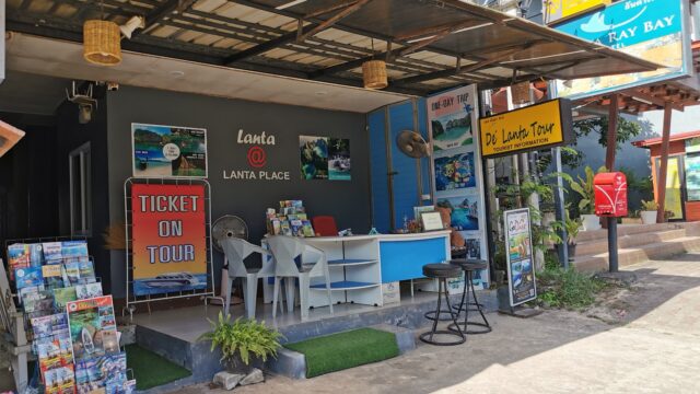 Outdoor travel agency office with brochures, a Ticket on Tour sign, plastic chairs, and colorful tour posters on display.