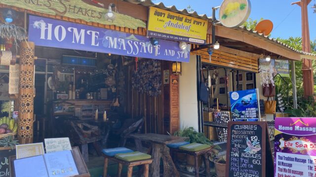 Outdoor view of a colorful massage and spa shop with signs, menus, and decorative items displayed at the entrance.