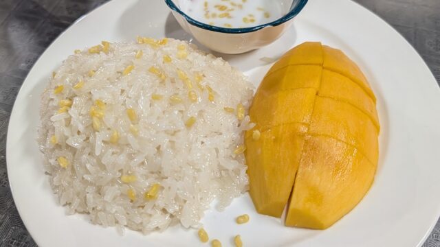 A plate with mango slices, sticky rice topped with mung beans, and a small dish of coconut sauce on a metal table.