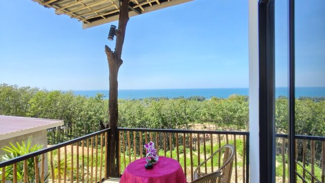 A balcony with two wicker chairs, a pink-covered table, and a scenic view of trees and blue sky.