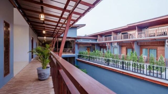 Modern two-story balcony with wooden railings and floors, potted plants, and rooms facing an open courtyard.