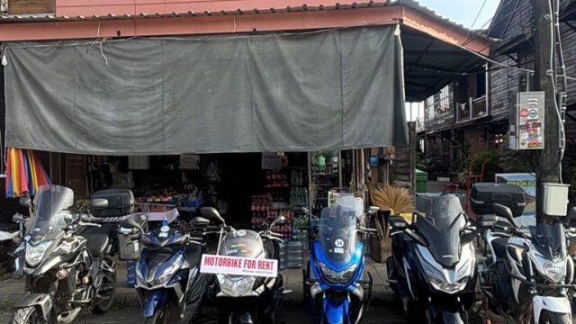 Six motorbikes parked outside a shop, with a Motorbike for Rent sign on the middle bike.