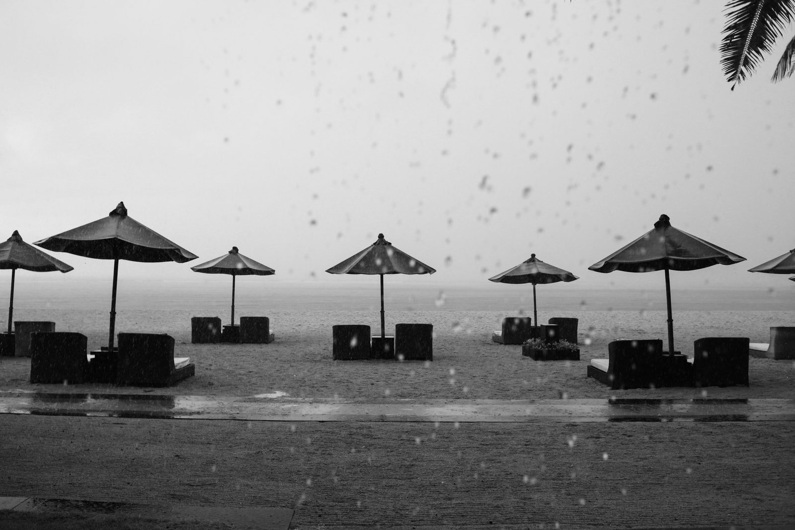 Heavy rain falling on a row of empty beach umbrellas and lounge chairs by the shore