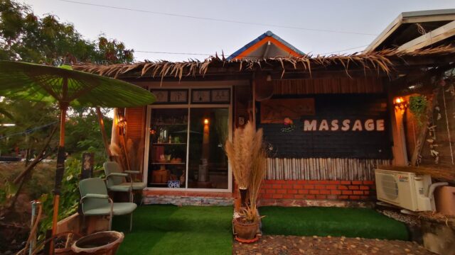A small massage shop with green artificial grass, potted plants, and cozy seating at the entrance during sunset.