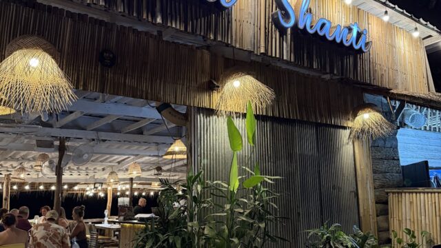 A bamboo-themed restaurant named Shanti Shanti is lit up at night, with plants and diners visible inside.