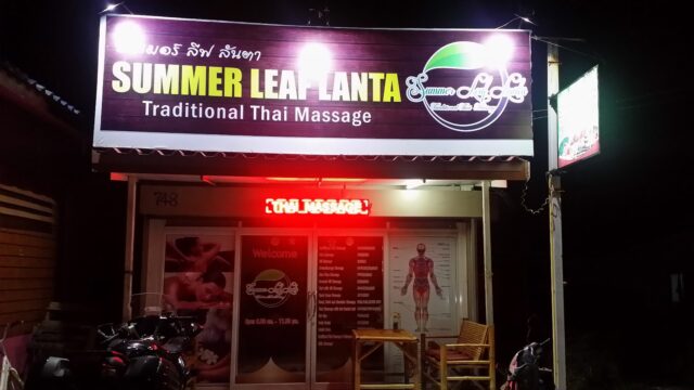A brightly lit storefront for SUMMER LEAF PLANTA Traditional Thai Massage with chairs and motorcycles outside at night.