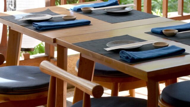 A wooden table set with plates, napkins, and utensils on a sunny patio at Sushi Miyuki.