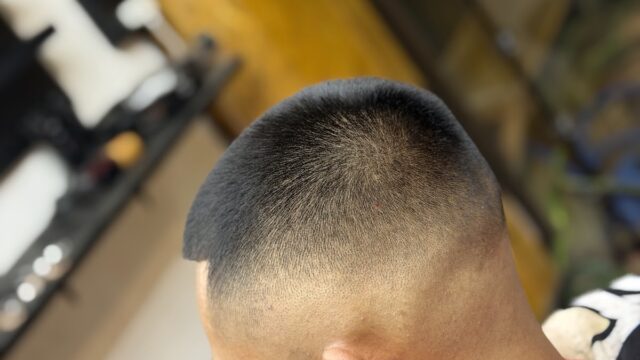A person with a fresh buzz cut and skin fade sits in a barber chair, wearing a colorful cape.
