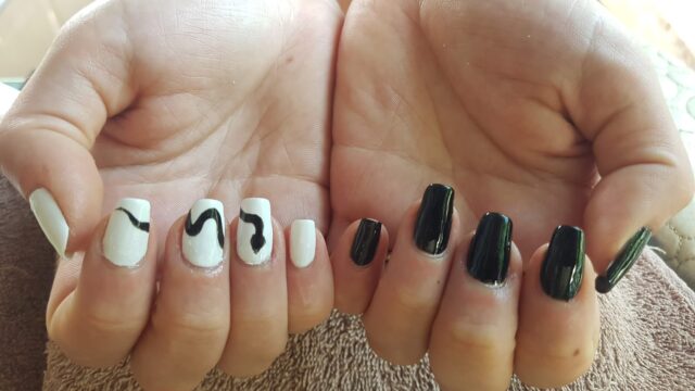 Two hands with manicured nails: one hand has black nails, the other white nails with black squiggly lines as decoration.